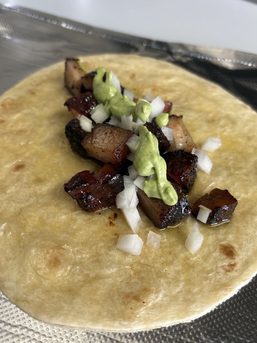 Pork belly burnt end taco with green crema and diced onion